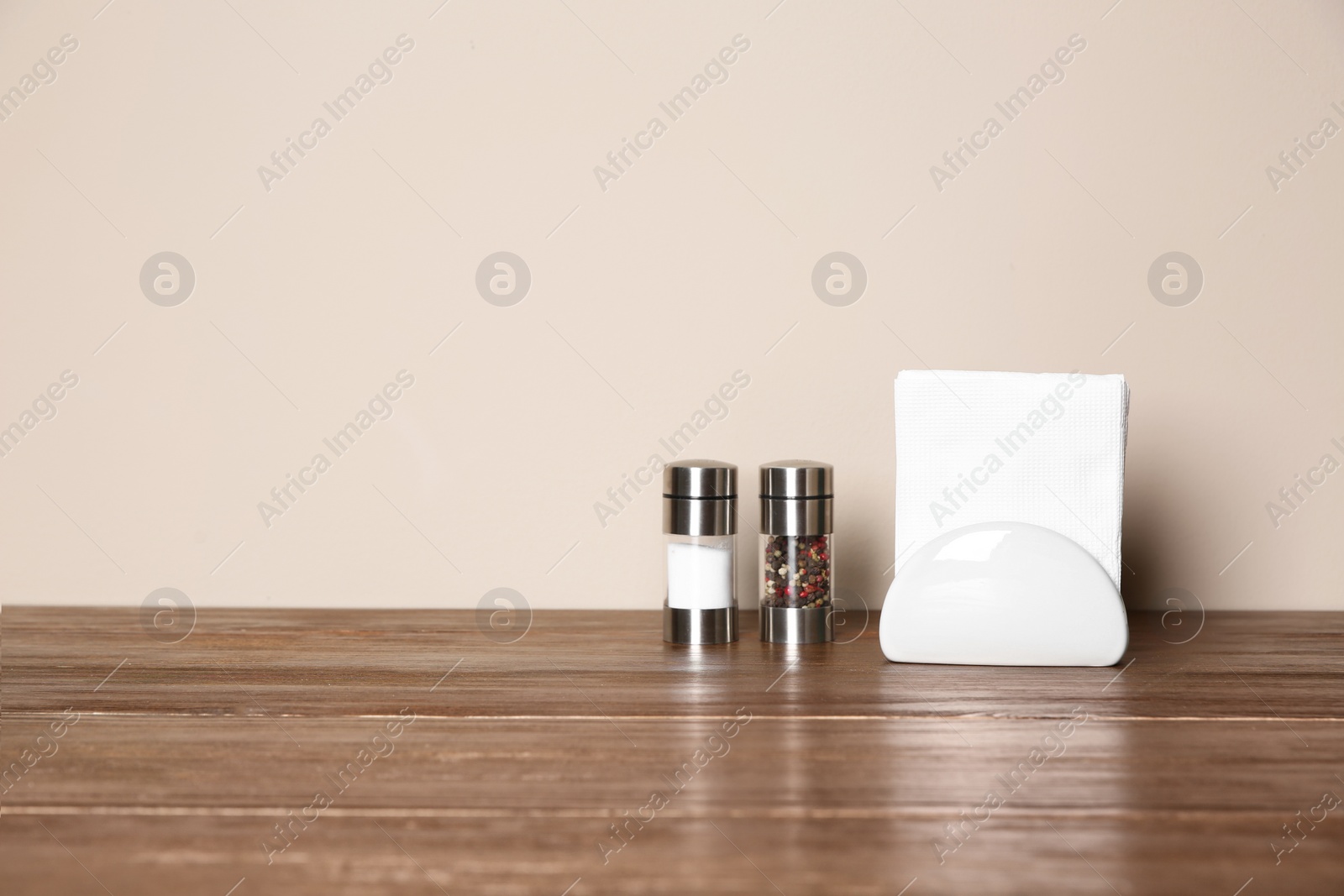 Photo of Napkin holder with salt and pepper shakers on table against color background. Space for text