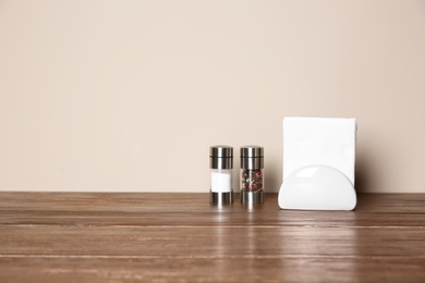 Photo of Napkin holder with salt and pepper shakers on table against color background. Space for text