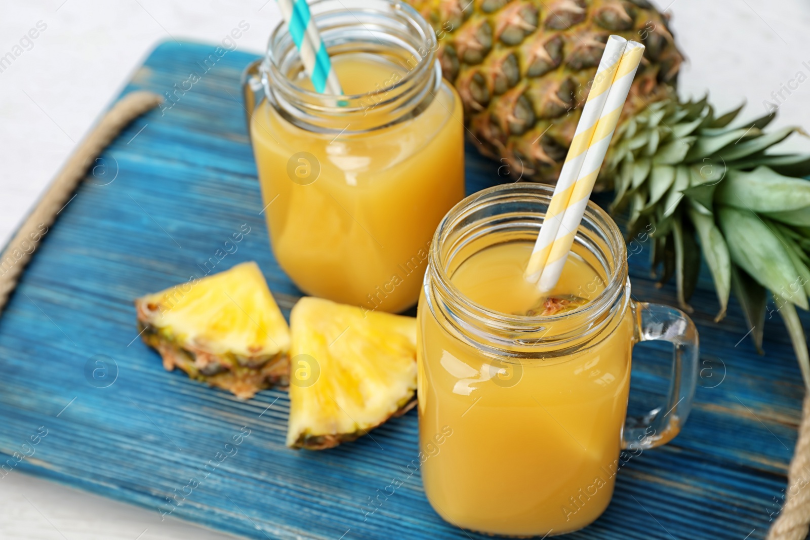 Photo of Mason jars with delicious pineapple juice on tray