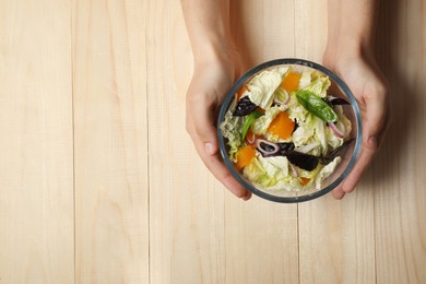 Woman holding bowl of delicious salad with Chinese cabbage, tomato and basil at wooden table, top view. Space for text