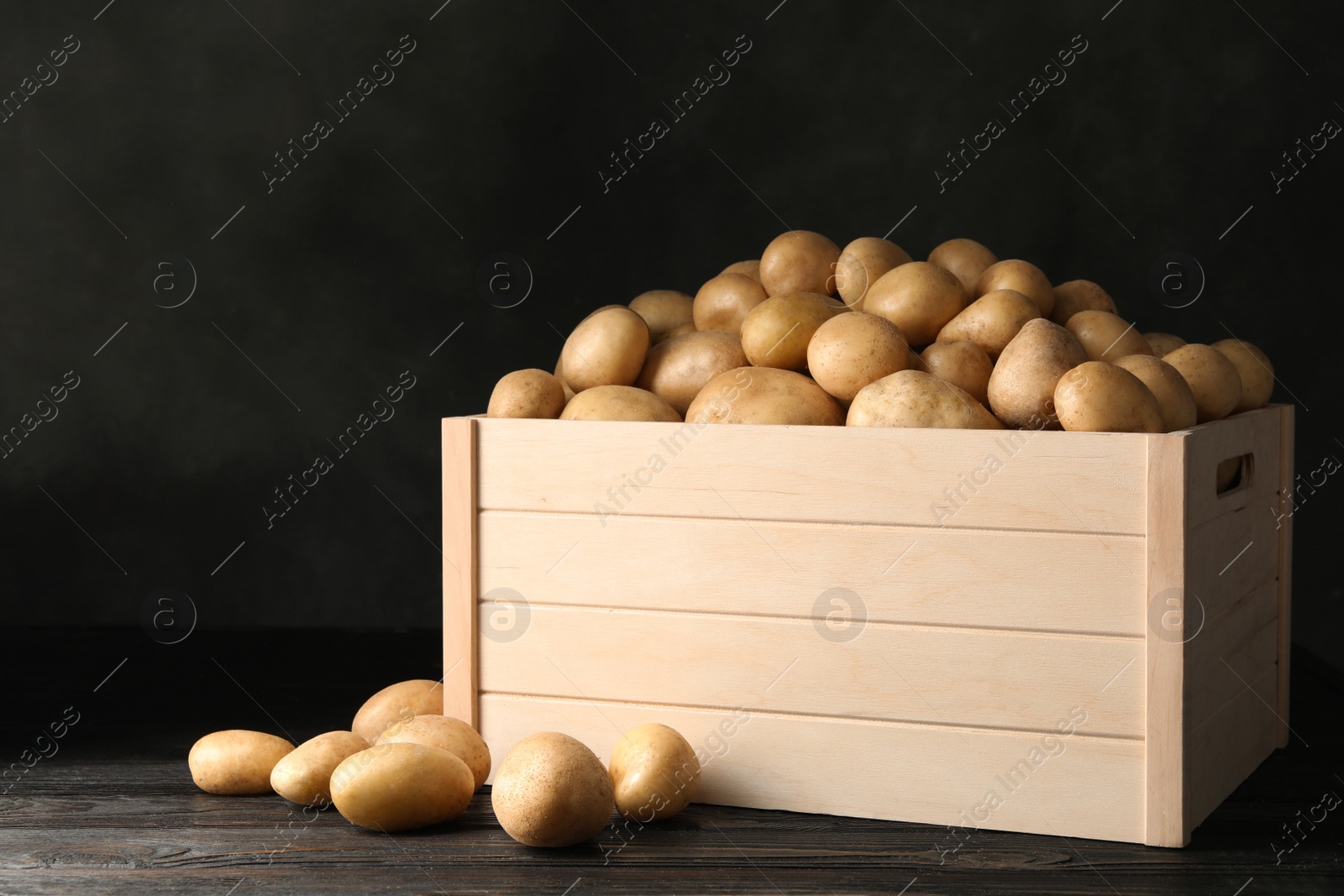 Photo of Raw fresh organic potatoes on wooden table against dark background