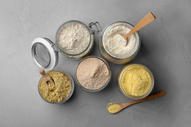 Jars with different types of flour on gray background