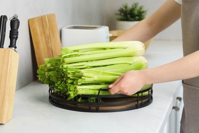 Photo of Woman with fresh green celery at white counter in kitchen, closeup