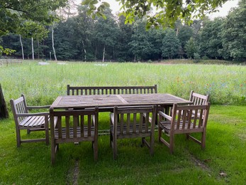 Wooden table with bench and chairs in garden. Landscape design