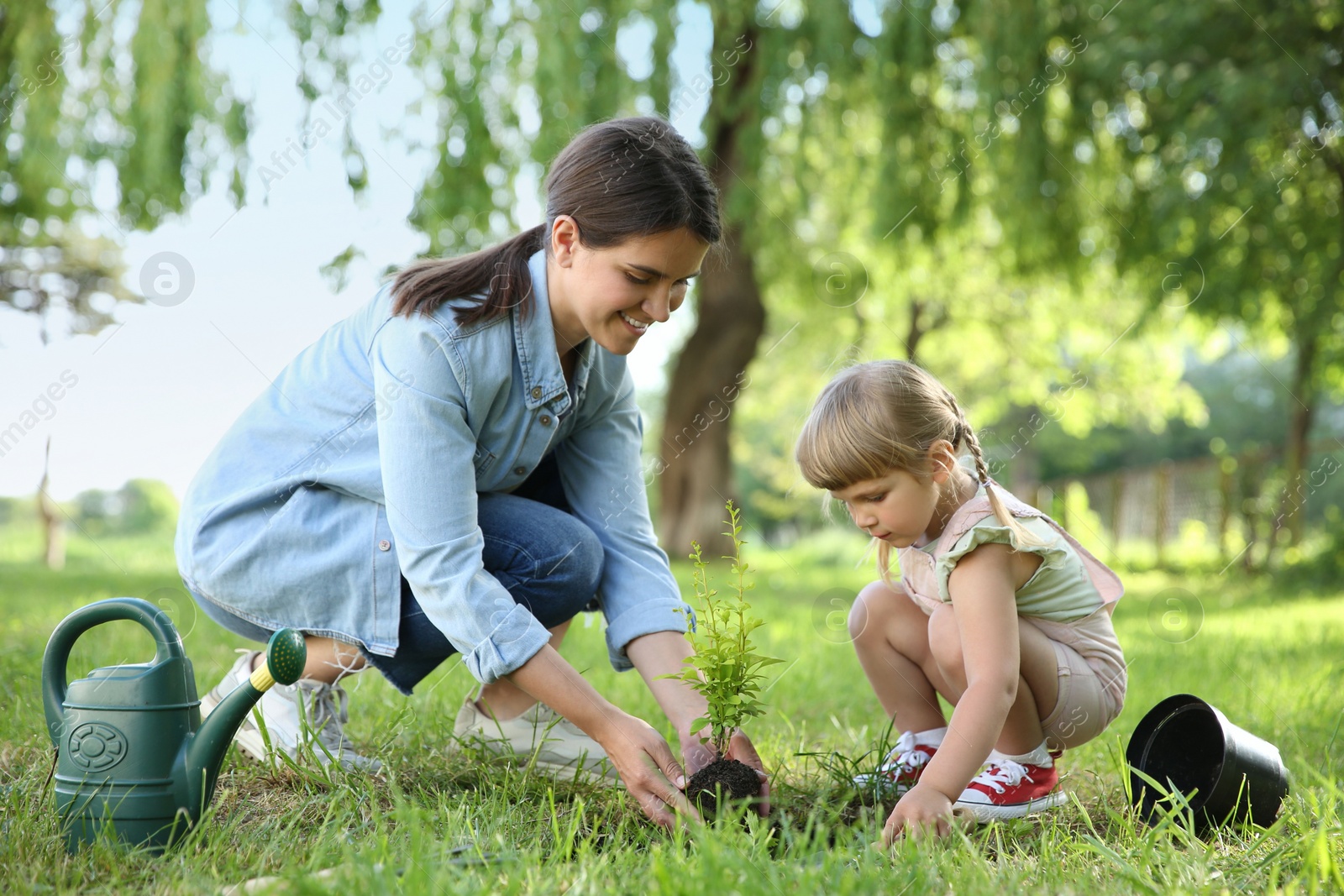 Photo of Mother and her daughter planting tree together in garden