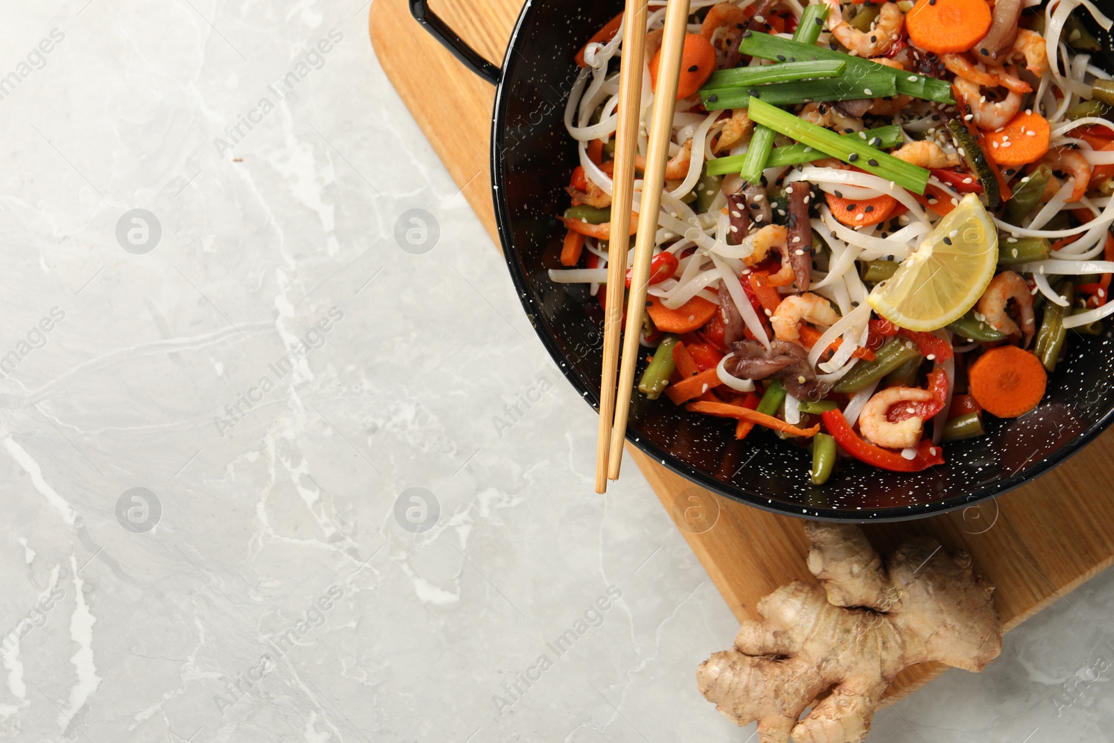 Photo of Shrimp stir fry with noodles and vegetables in wok on grey table, top view. Space for text