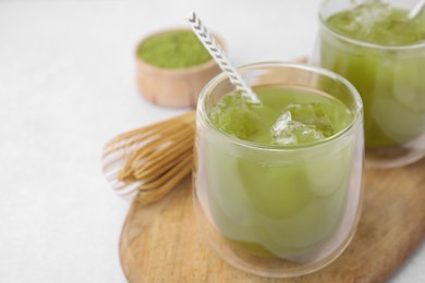 Photo of Delicious iced green matcha tea and bamboo whisk on white table, closeup. Space for text