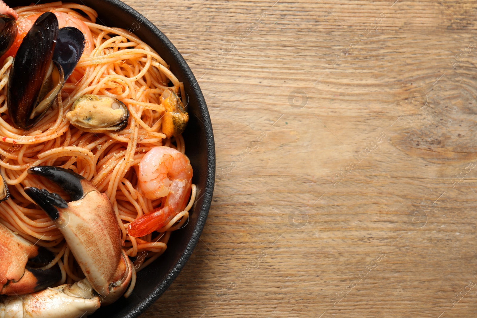 Photo of Delicious spaghetti with seafood served on wooden table, top view. Space for text