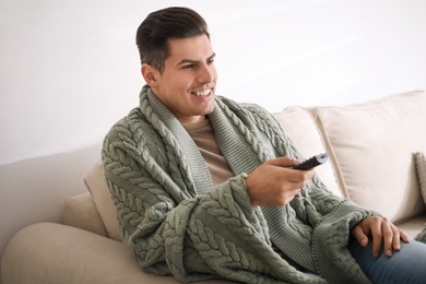 Man covered with warm green plaid watching television on sofa at home