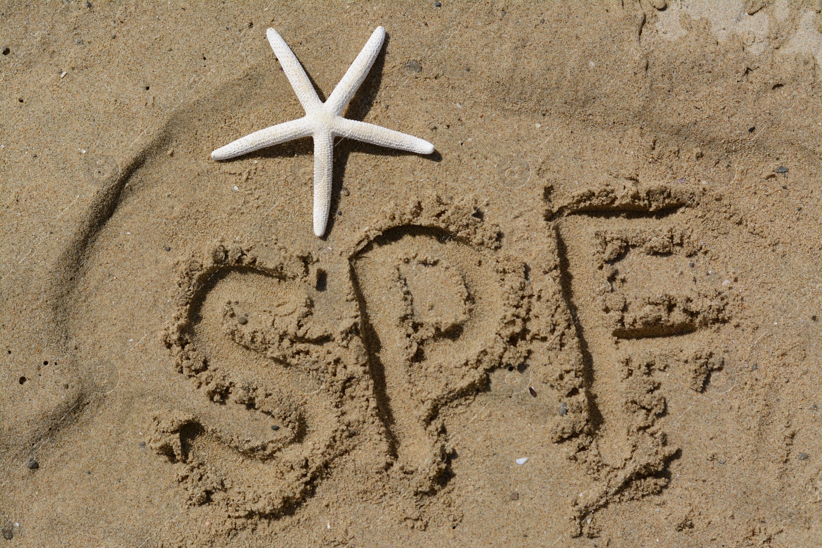 Photo of Abbreviation SPF written on sand and starfish at beach, top view