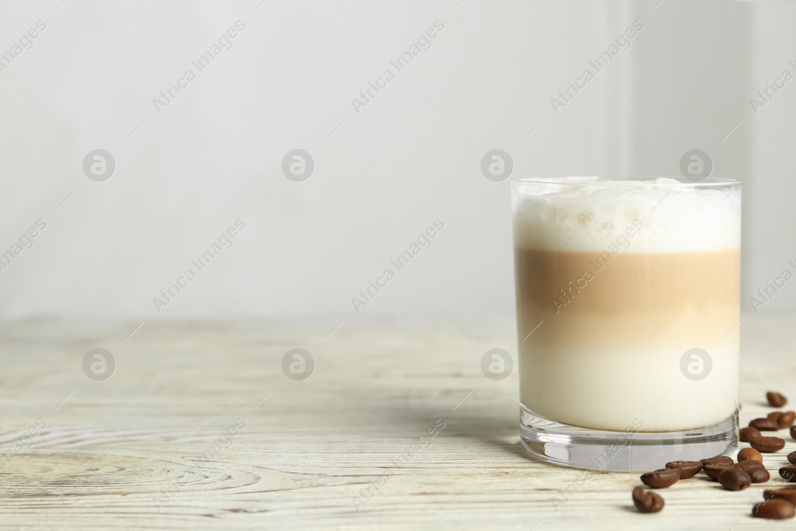 Photo of Delicious latte macchiato and coffee beans on white wooden table indoors, space for text