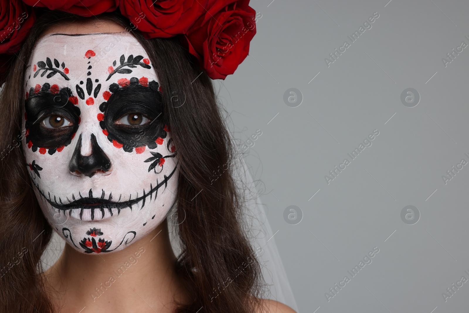 Photo of Young woman in scary bride costume with sugar skull makeup and flower crown on light grey background, closeup and space for text. Halloween celebration