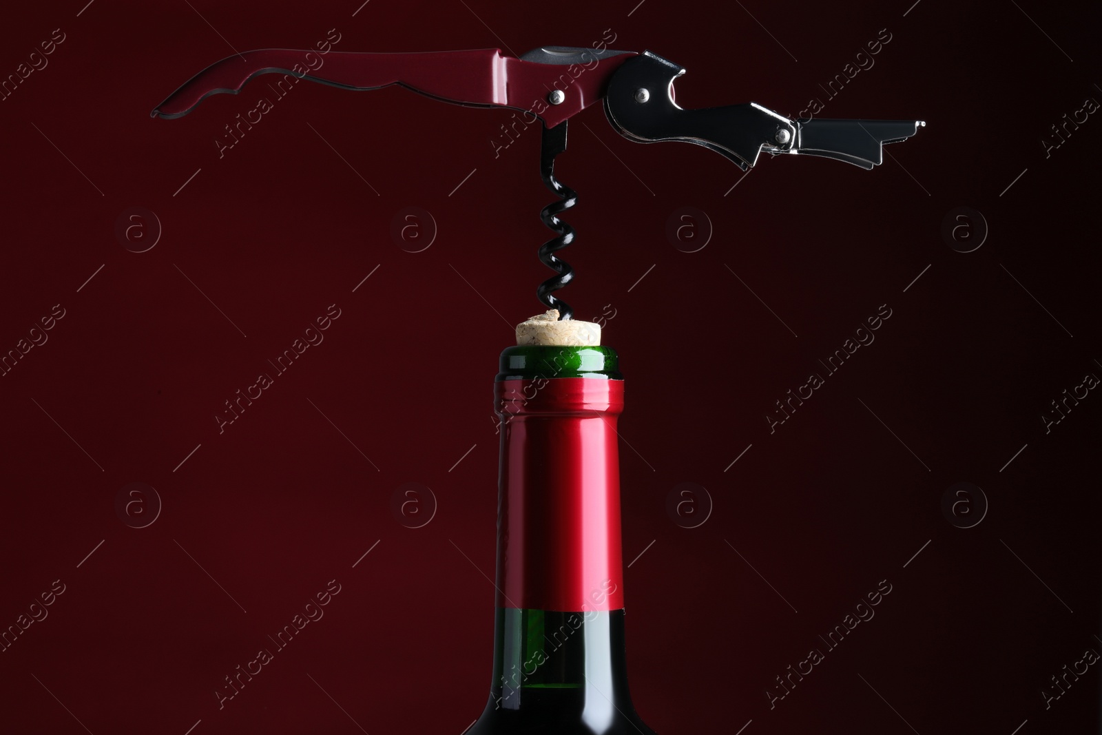 Photo of Opening bottle of wine with corkscrew on burgundy background