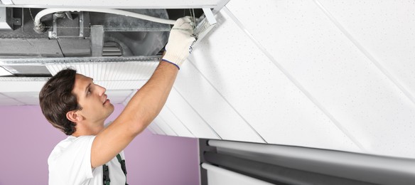 Image of Young male technician repairing air conditioner indoors, space for text. Banner design