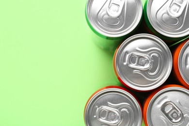 Energy drink in cans on light green background, top view. Space for text