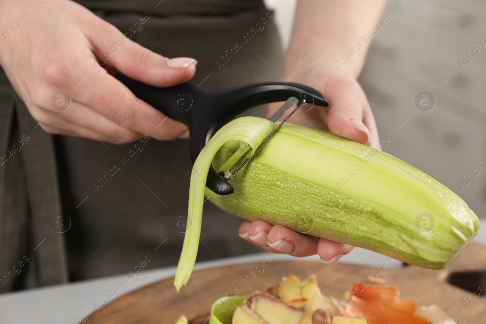 Photo of Woman peeling fresh zucchini at table indoors, closeup