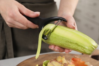 Photo of Woman peeling fresh zucchini at table indoors, closeup