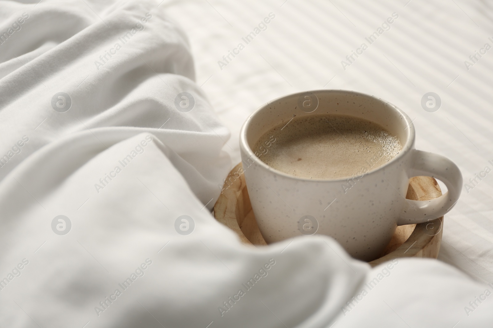 Photo of Cup of aromatic coffee on bed with soft blanket, closeup. Space for text