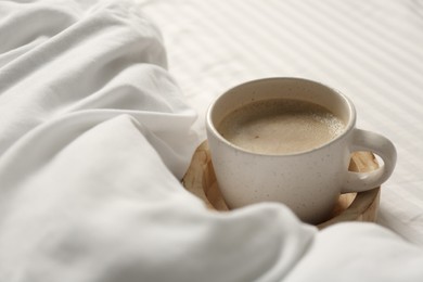 Cup of aromatic coffee on bed with soft blanket, closeup. Space for text