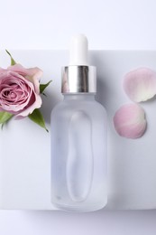 Photo of Bottle of cosmetic serum, beautiful rose flower and petals on white background,top view