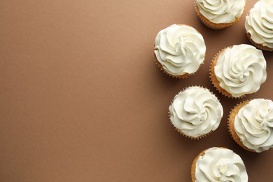 Photo of Tasty vanilla cupcakes with cream on dark beige background, top view. Space for text