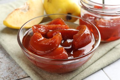 Tasty homemade quince jam in bowl on tiled table, closeup