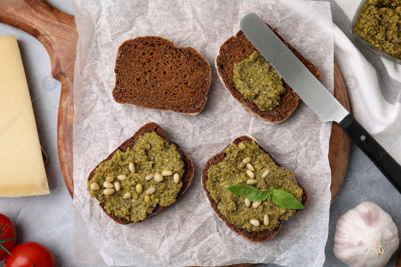 Photo of Making delicious bruschettas with pesto sauce, nuts and fresh basil on light grey table, flat lay