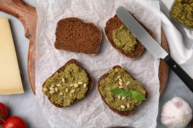 Photo of Making delicious bruschettas with pesto sauce, nuts and fresh basil on light grey table, flat lay