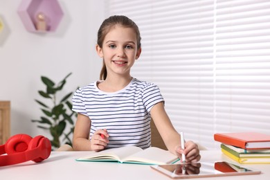 Photo of E-learning. Cute girl using tablet for studying online at table indoors