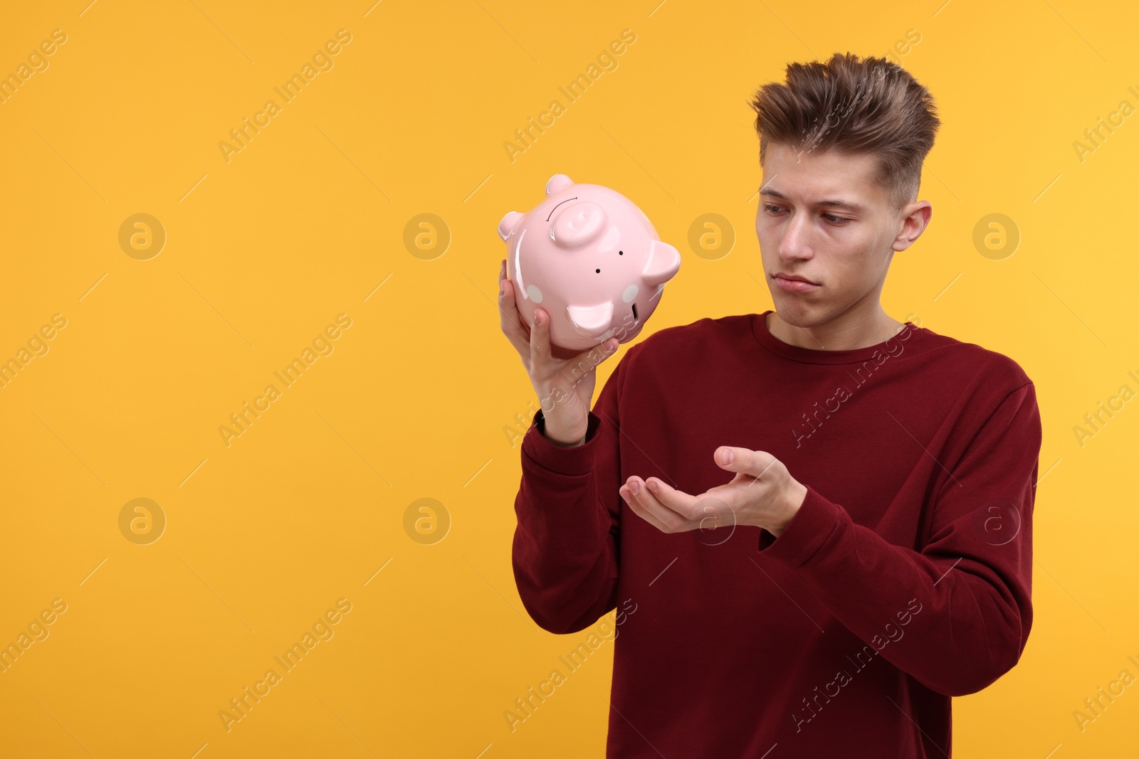 Photo of Upset man with empty piggy bank on yellow background. Space for text