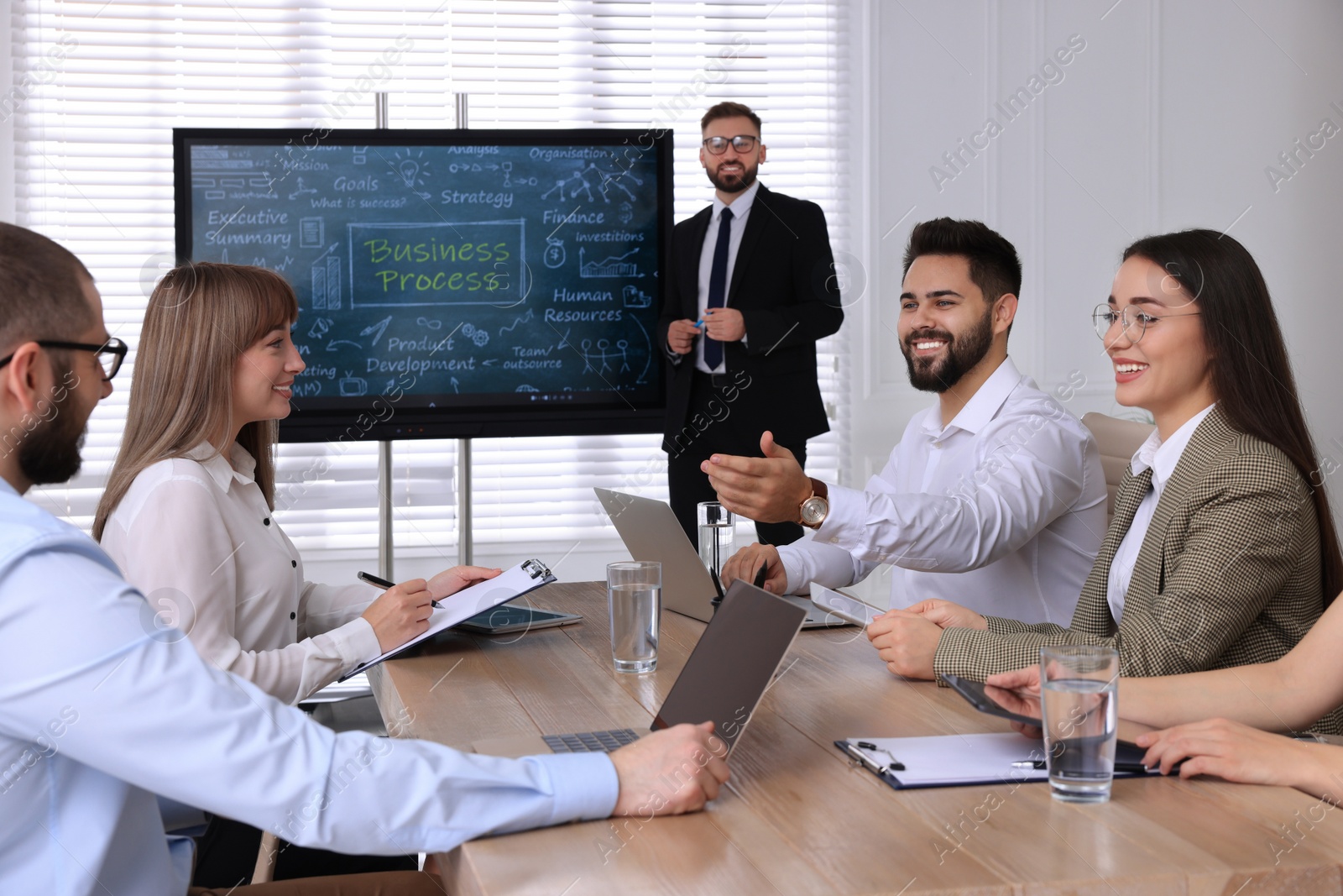 Photo of Business trainer near interactive board in meeting room during presentation, focus on colleagues