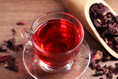 Photo of Cup of fresh hibiscus tea and dry flower leaves on wooden table, closeup