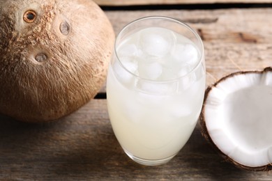 Photo of Glass of coconut water, ice cubes and nuts on wooden table