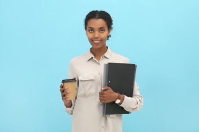 Photo of African American intern with folders and coffee on light blue background