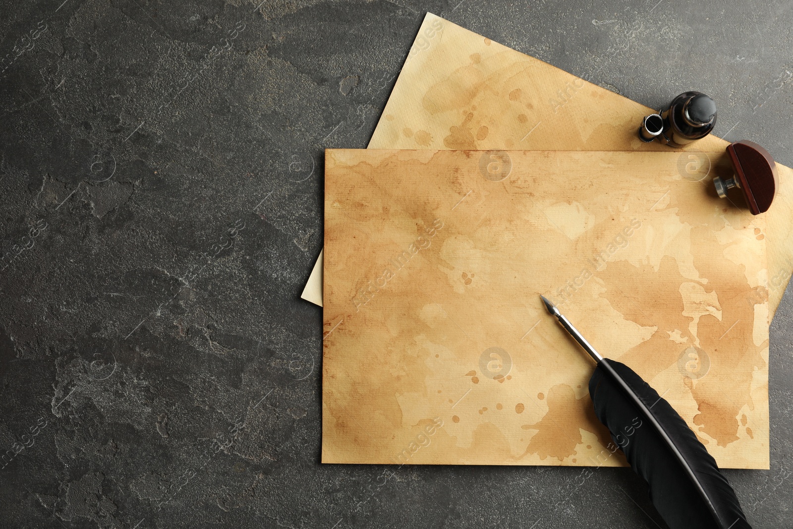 Photo of Black feather, inkwell and vintage parchment on grey table, flat lay