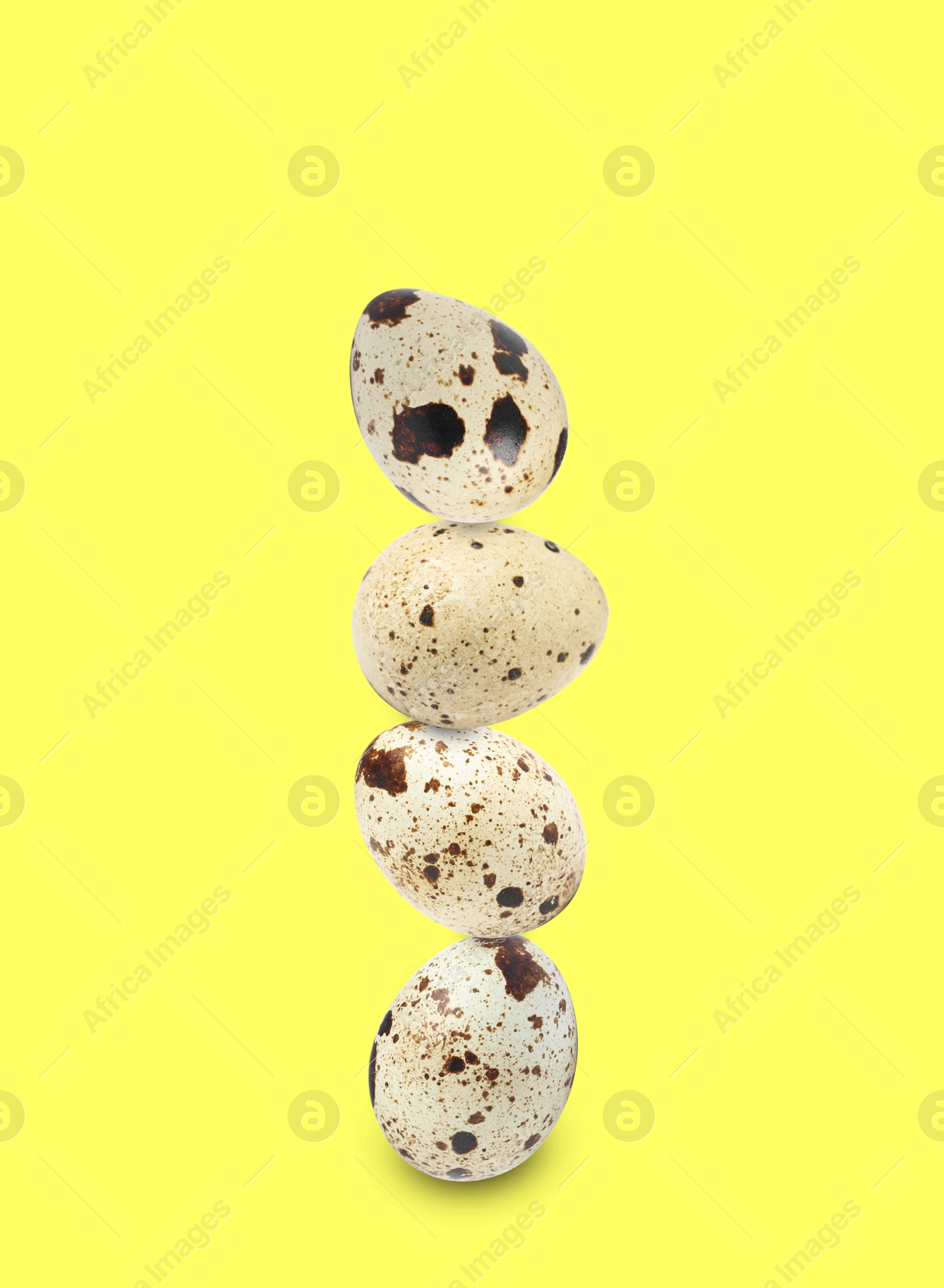 Image of Stacked speckled quail eggs on light yellow background