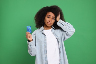 Confused woman with credit card on green background. Debt problem