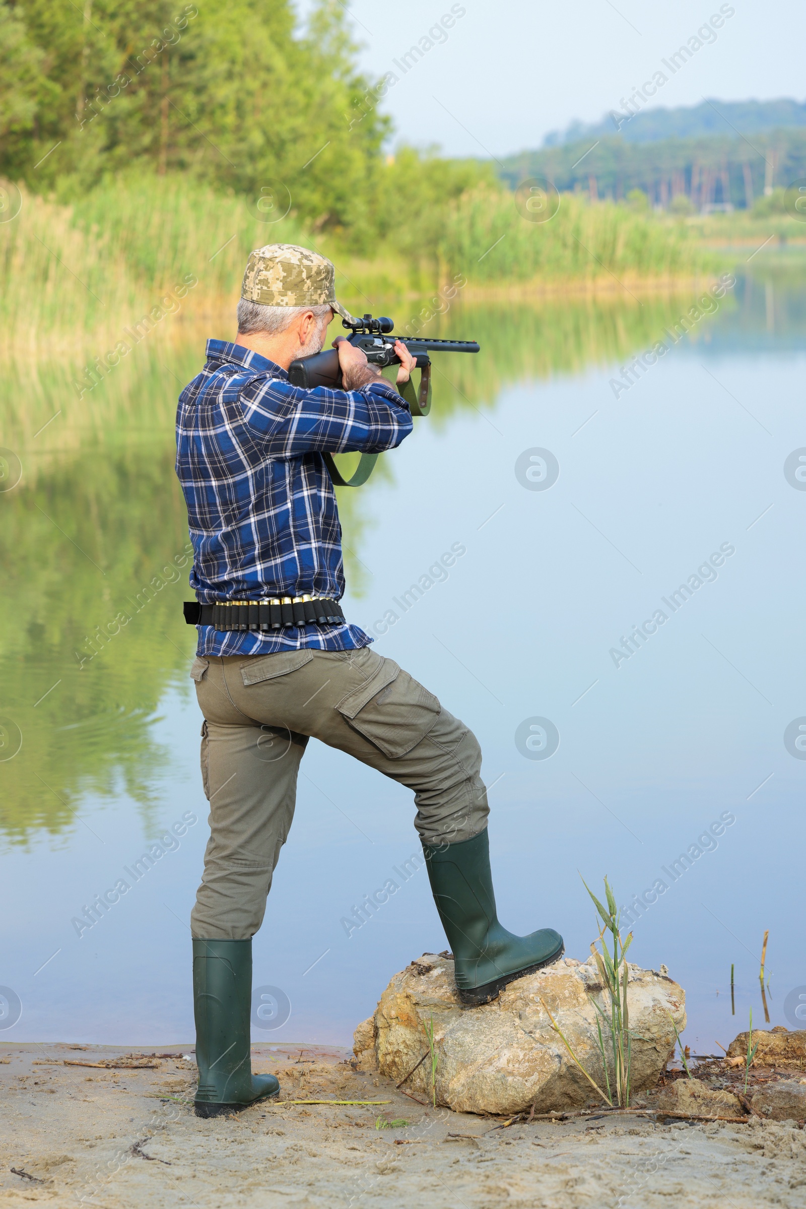 Photo of Man aiming with hunting rifle near lake outdoors
