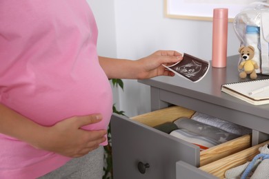 Pregnant woman holding ultrasound photo of baby at home, closeup