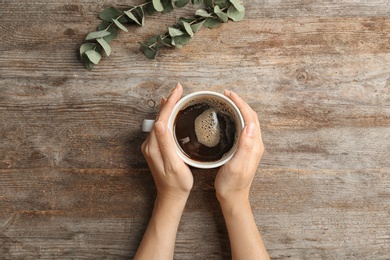 Photo of Young woman with cup of delicious hot coffee on wooden background, top view