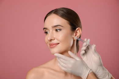Beautiful woman getting facial injection on pink background. Cosmetic surgery