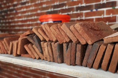 Photo of Many decorative bricks on scaffolding near wall, closeup. Tiles installation process