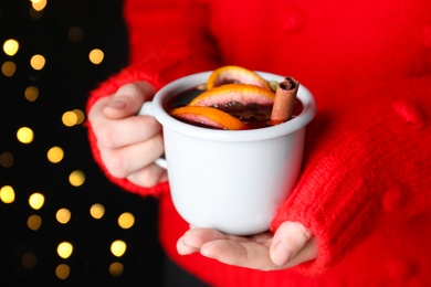Woman holding cup of mulled wine against blurred lights, closeup