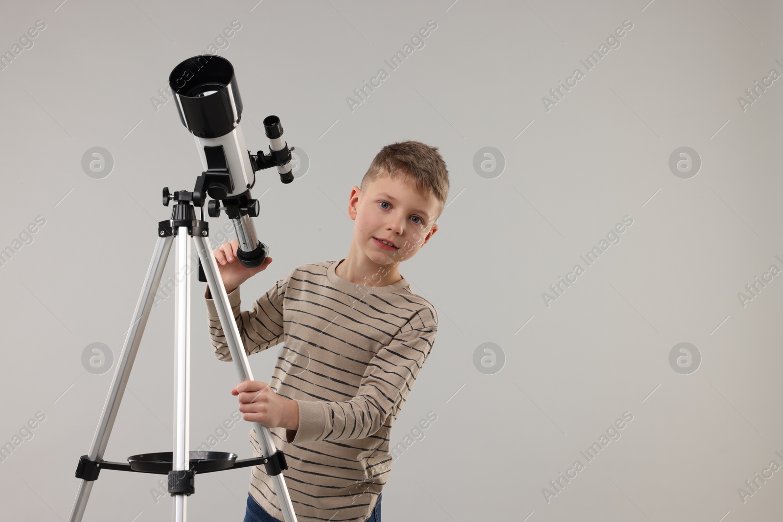 Photo of Cute little boy with telescope on light grey background, space for text