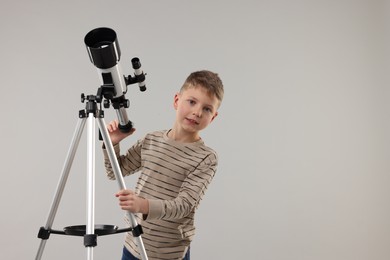 Cute little boy with telescope on light grey background, space for text