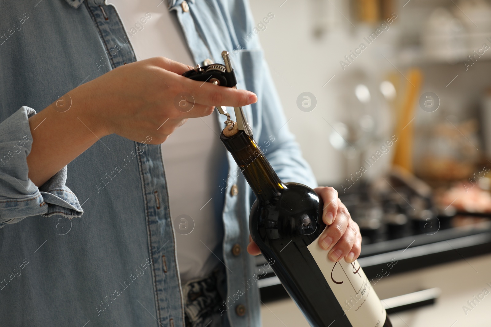 Photo of Woman opening wine bottle with corkscrew indoors, closeup. Space for text