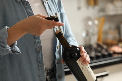 Woman opening wine bottle with corkscrew indoors, closeup. Space for text