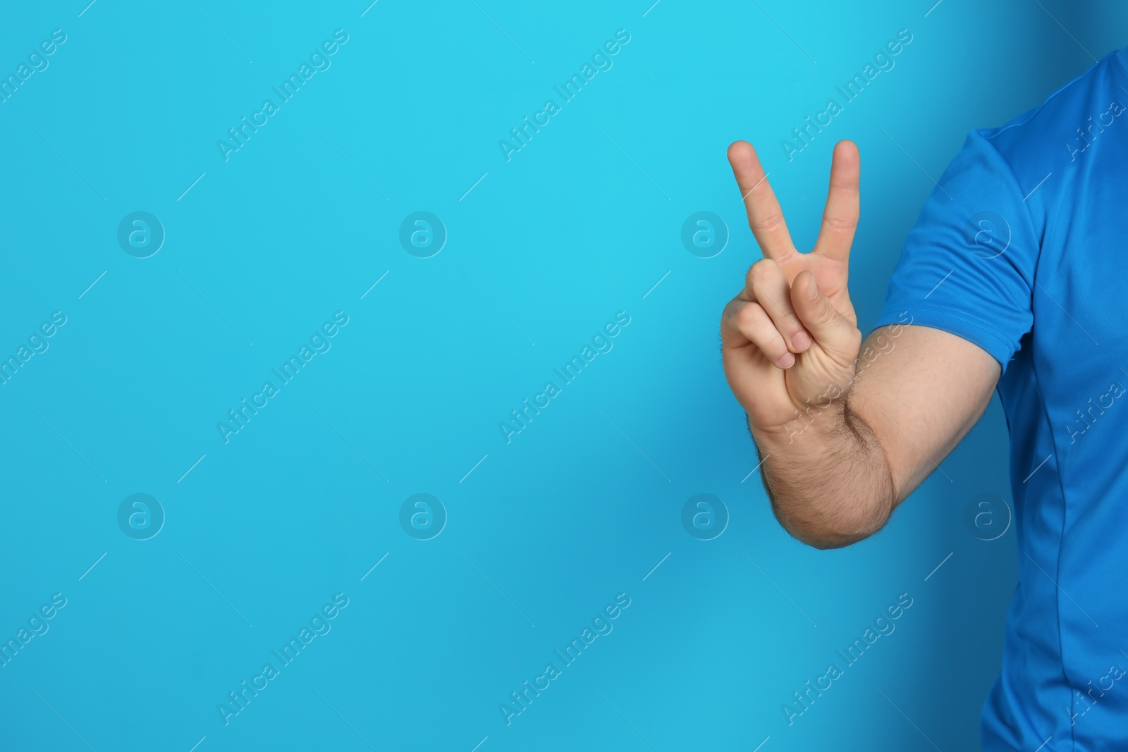 Photo of Young man showing victory gesture on color background. Space for text