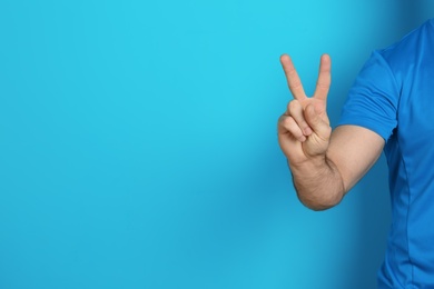 Young man showing victory gesture on color background. Space for text