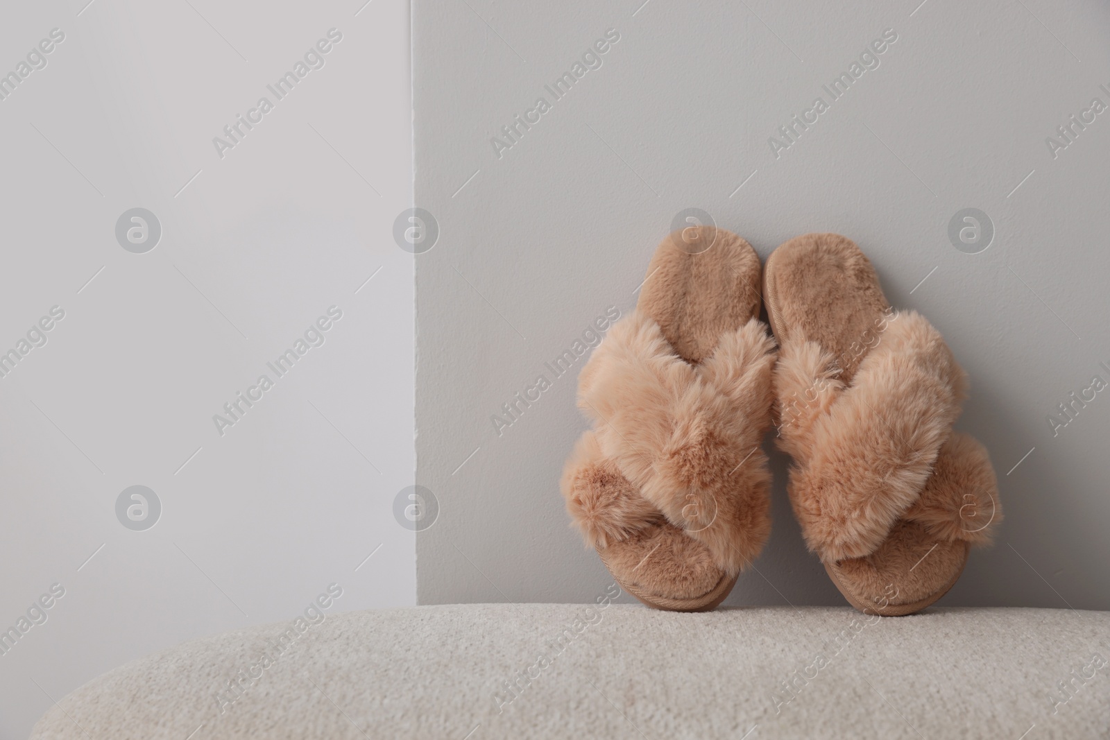 Photo of Soft beige slippers near grey wall, space for text